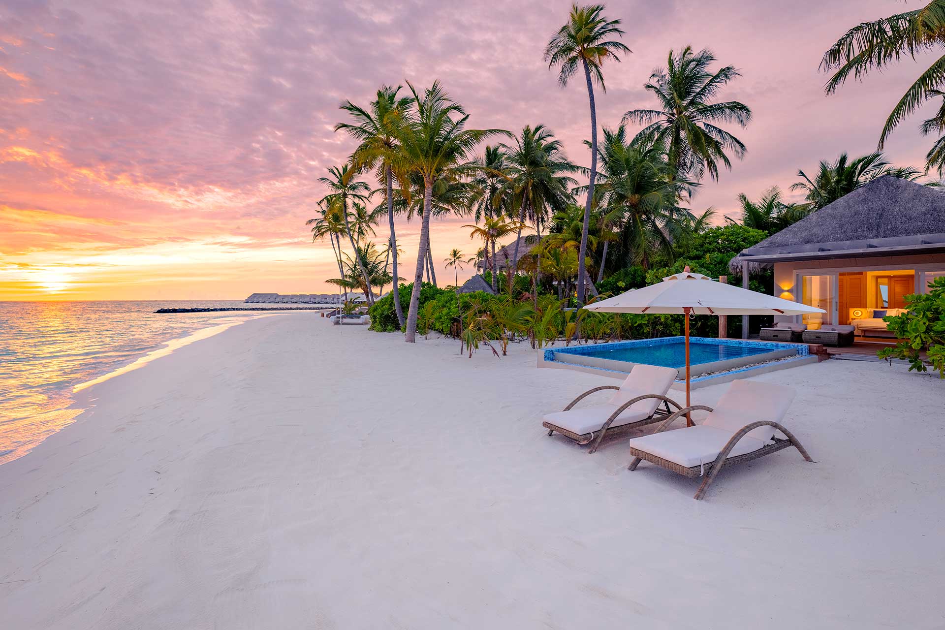 Sunset over private beach villa at Baglioni Resort Maldives with pink and gold sky, palm trees and pool